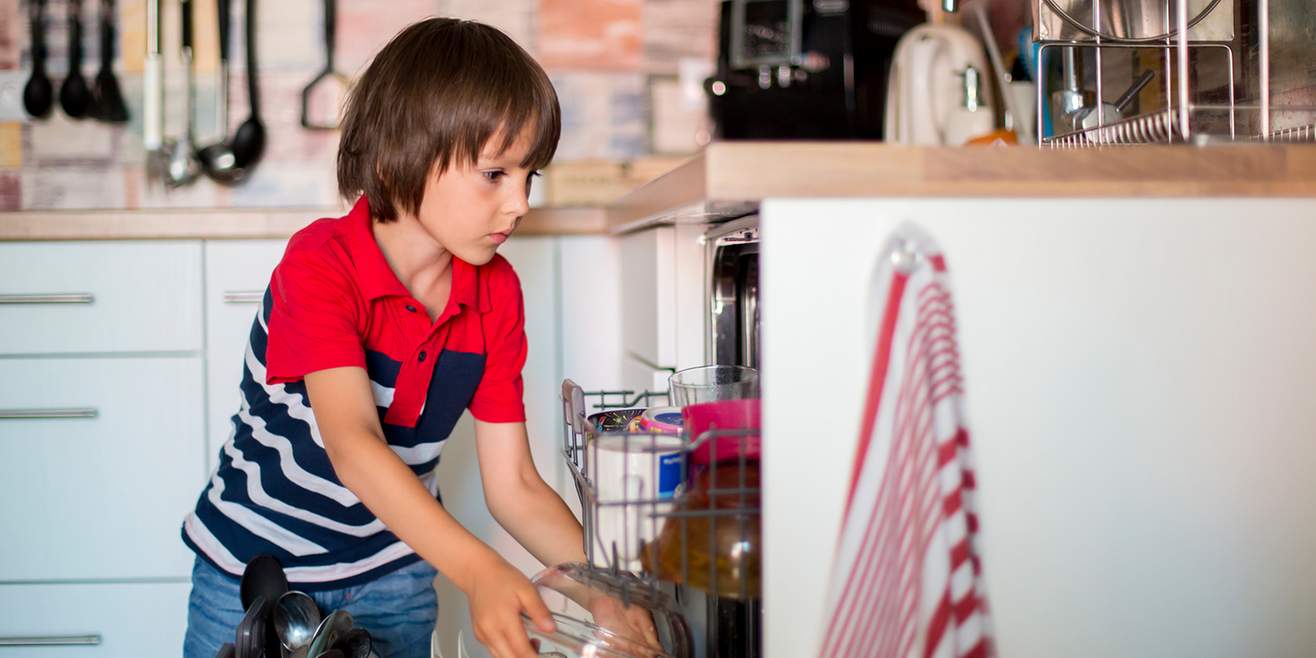 Un garçon en train de remplir le lave-vaisselle.
