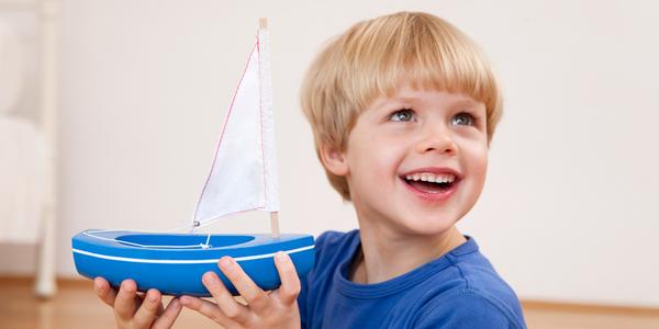 Bimbo sorridente con in mano una barca a vela giocattolo
