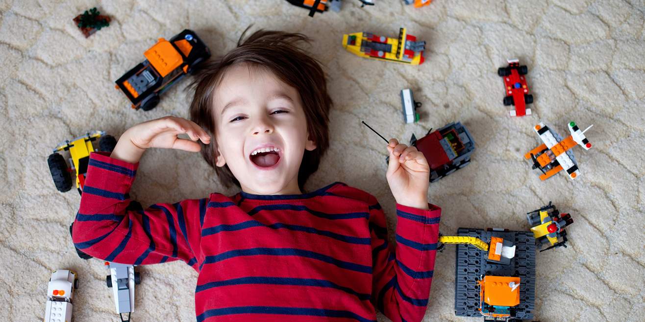Bambino felice disteso a terra circondato da giocattoli